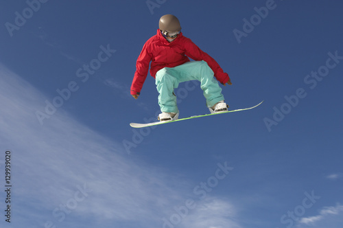 Low angle view of young male snowboarder in winter clothes jumping against sky