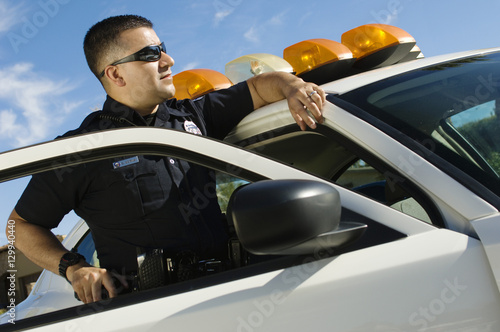 Fotografie Male police officer with gun leaning on patrol car