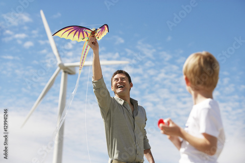 Father and son playing with dragon kite near turbine at wind farm