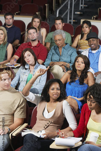 Portrait of a young female student raising hand to answer a question in the classroom