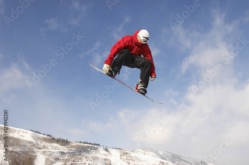 Low angle view of young male snowboarder jumping against cloudy sky