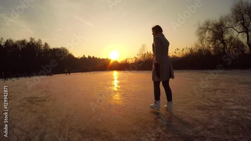 CLOSE UP: Young woman iceskating fast on big frozen pond in local park at sunset