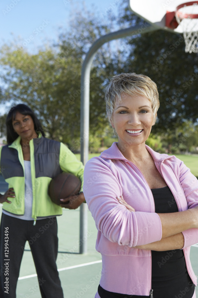 Portrait of a beautiful woman standing at outdoor basketball court with friend in background