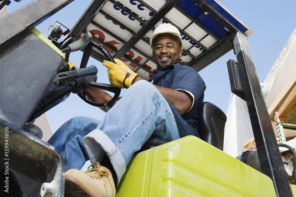Low angle view of a happy African American industrial worker driving forklift Low angle view of a happy African American industrial worker driving forklift