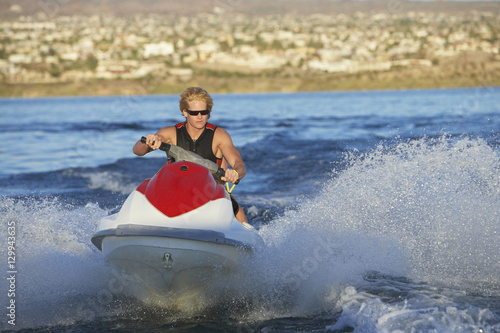 Young Caucasian man riding personal watercraft on lake © moodboard