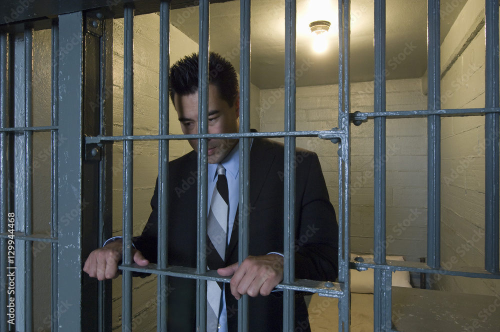 Japanese businessman standing behind bars in prison cell Japanese businessman standing behind bars in prison cell