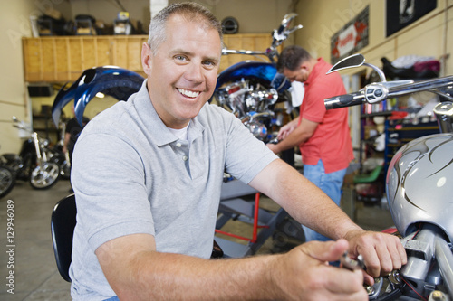 Portrait of a happy mechanic working on motorcycle with his coworker in the background