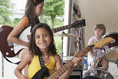 Portrait of cheerful young girl playing guitar with band in garage