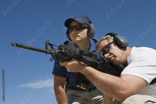 Low angle view of instructor with man aiming machine gun at firing range