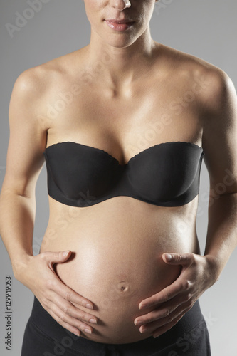 Midsection of pregnant woman with hands over tummy on gray background