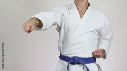On a gray background athlete in a white kimono with a blue belt making punch