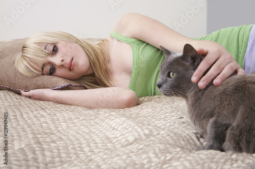 Teenage girl looking at cat while lying in bed at home © moodboard