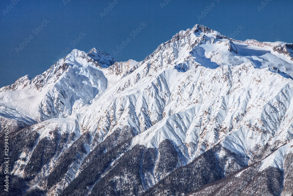 Beautiful scenic winter landscape of the Main Caucasus ridge with snowy mountain peak tops on blue sky background