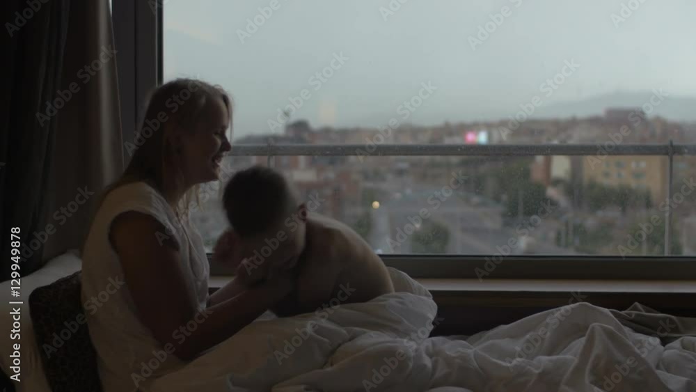 Happy mother and son lying in bed near the window and having fun Happy mother and son lying in bed near the window and having fun