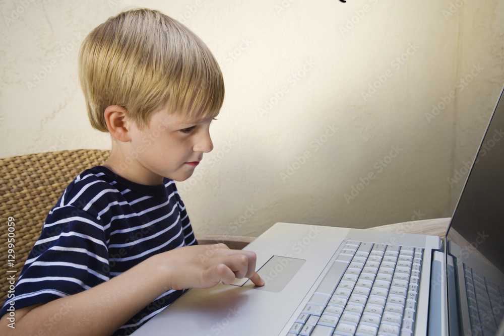 Cute little boy using laptop while sitting on chair Cute little boy using laptop while sitting on chair
