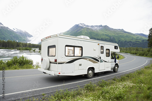 Recreational vehicle passing through a lakeside road with mountain in background, Alaska, USA
