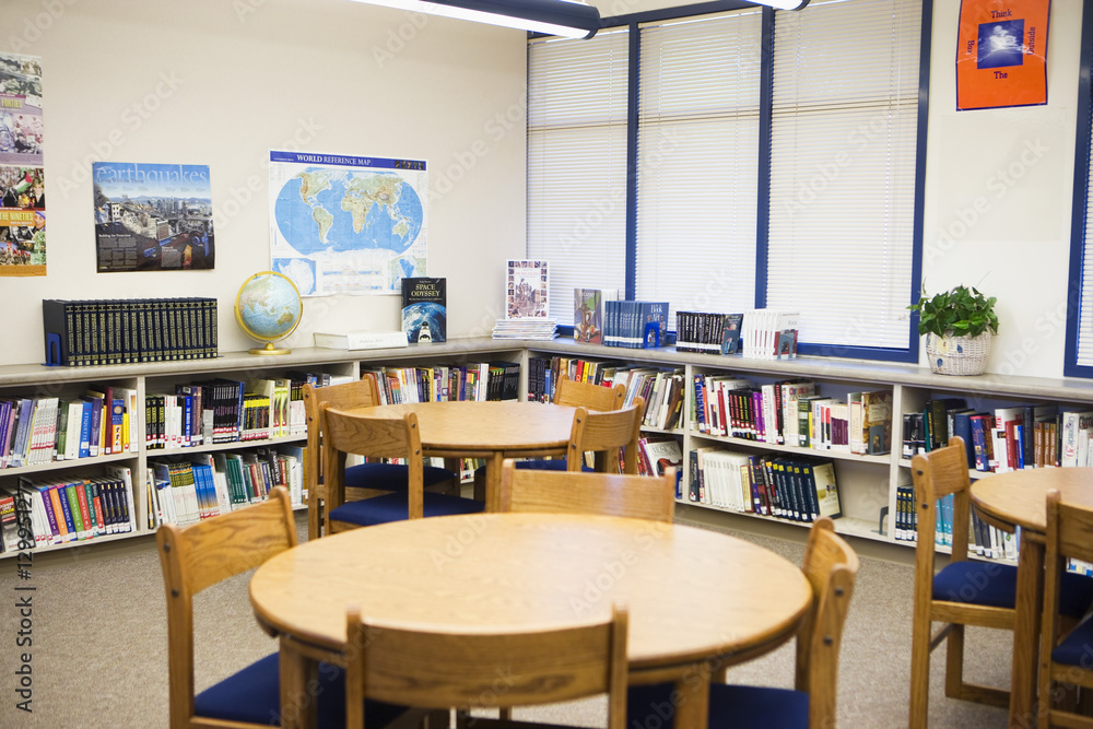 Tables and chairs with books arranged on shelves in high school library Tables and chairs with books arranged on shelves in high school library