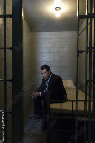 Depressed young businessman sitting on bed in prison