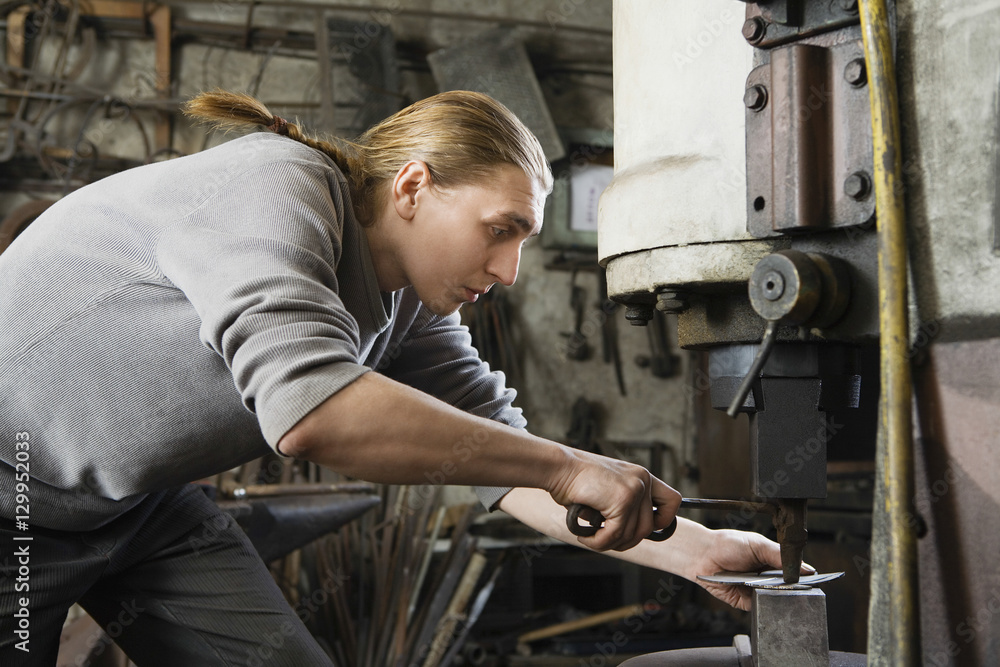 Young male blacksmith working in workshop Young male blacksmith working in workshop