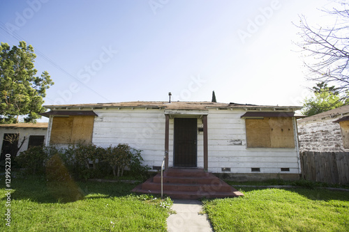 Abandoned house with boarded up windows and green lawn © moodboard