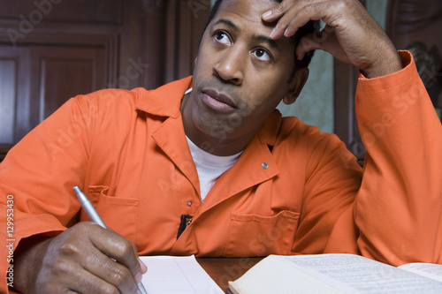 Fotografija Contemplative male criminal writing on paper in courtroom
