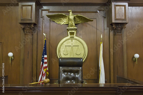 Legal scales with flags behind judge's chair in courtroom photo