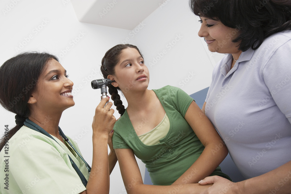 Happy female doctor checking girl's ear as she to the patient's mother