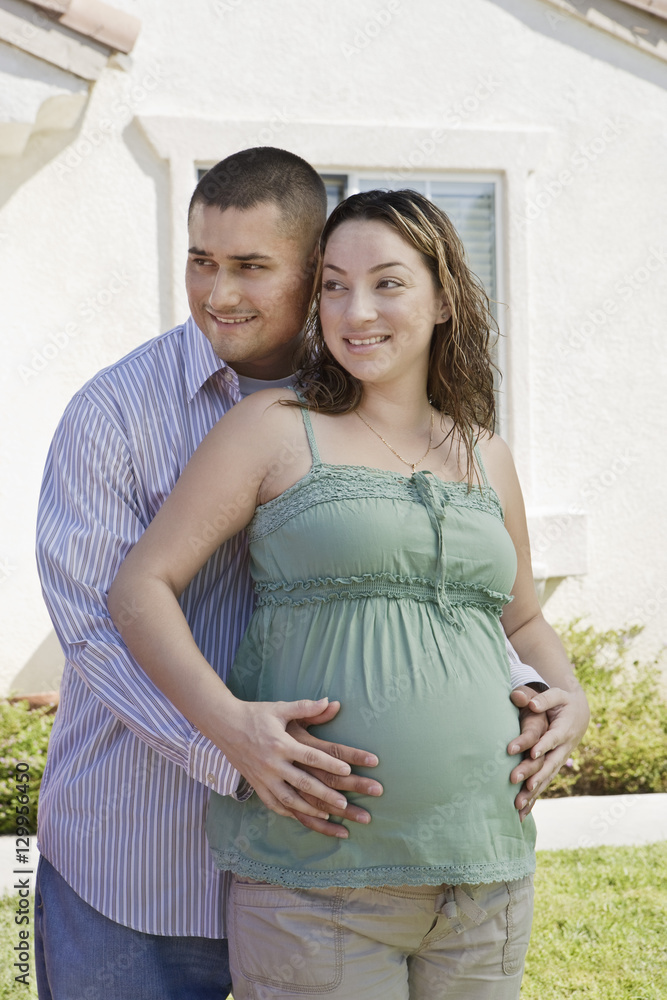 Man standing behind expecting woman and holding her belly Man standing behind expecting woman and holding her belly