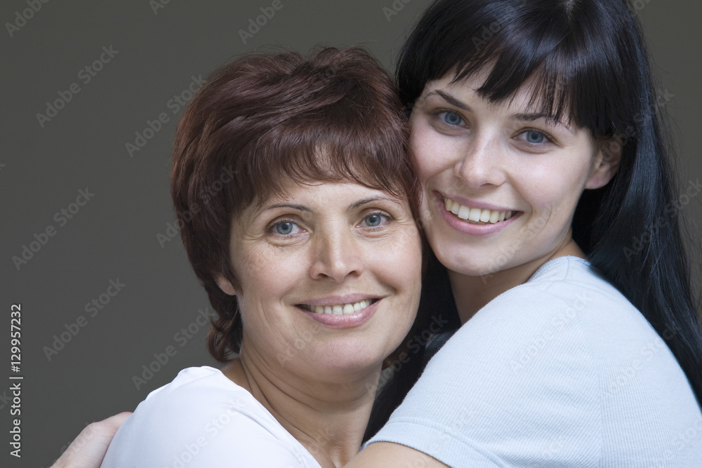 Closeup of a smiling young woman embracing her mother against gray background Closeup of a smiling young woman embracing her mother against gray background