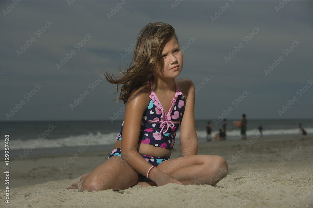 Sad little girl sitting on sand at a beach Sad little girl sitting on sand at a beach