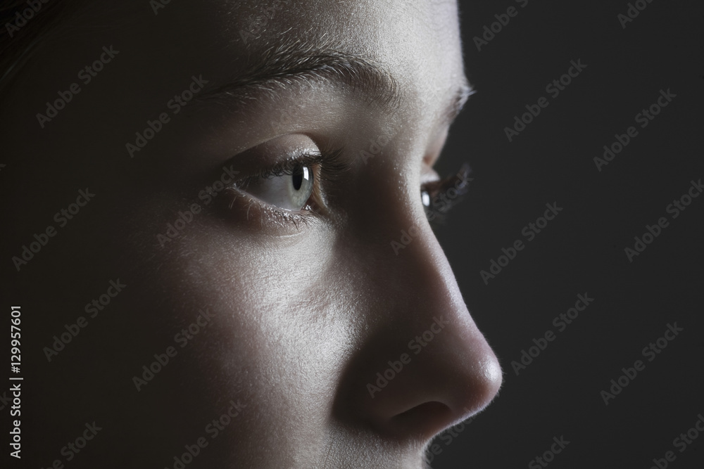 Closeup side view of a teenage girl looking away against black ...