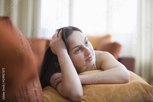 Thoughtful young woman lying on sofa as she looks up