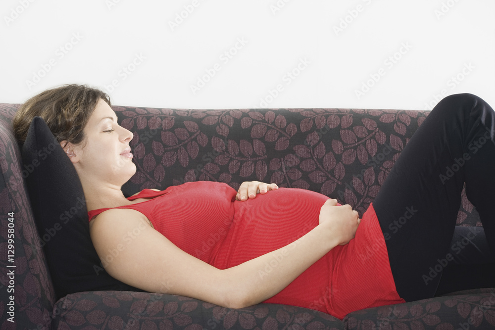 Side view of a pregnant young woman sleeping on sofa at home