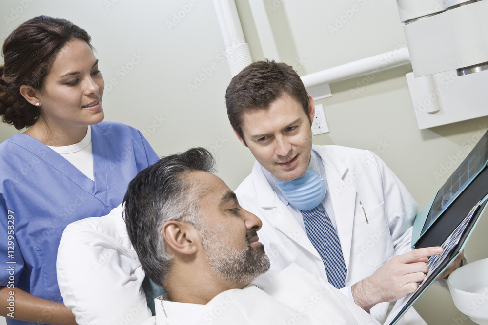 Fototapeta premium Male dentist with nurse explaining x-ray report to patient in clinic