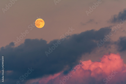 An orange full moon rises above magenta clouds.
