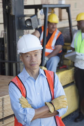Portrait of warehouse manager with arms crossed and colleagues in background