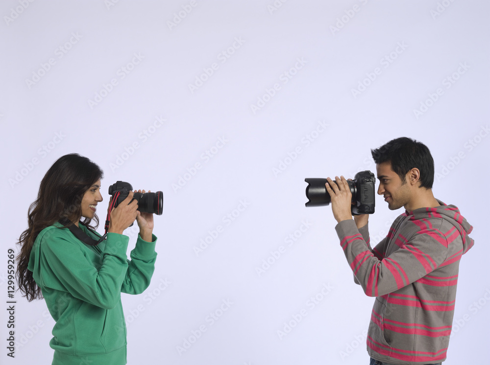 Side view of a woman and young man photographing each other in studio