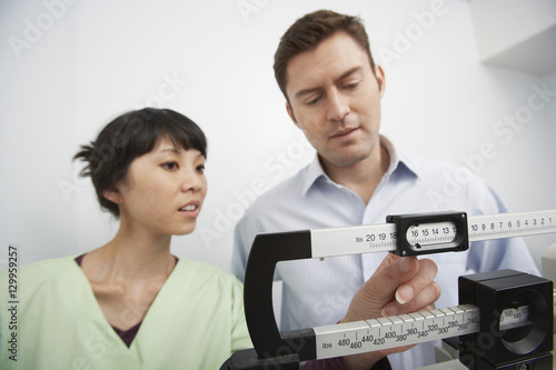 Fotografija An Asian female nurse adjusting weighing scale for man at clinic