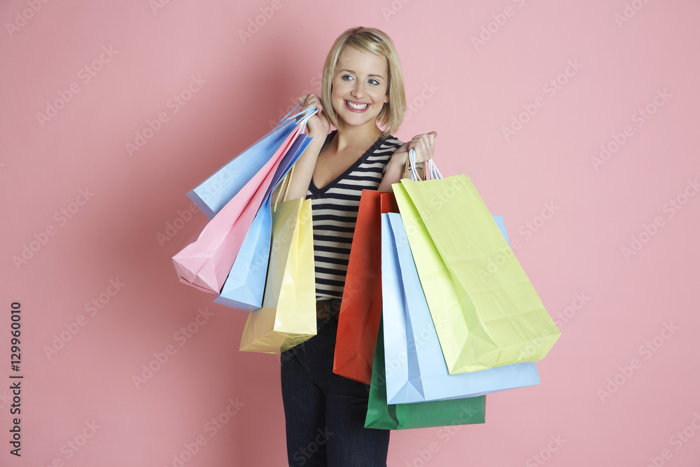 Happy shopaholic woman carrying shopping bags isolated over pink background