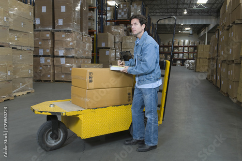 Full length side view of a man operating trolley in distribution warehouse