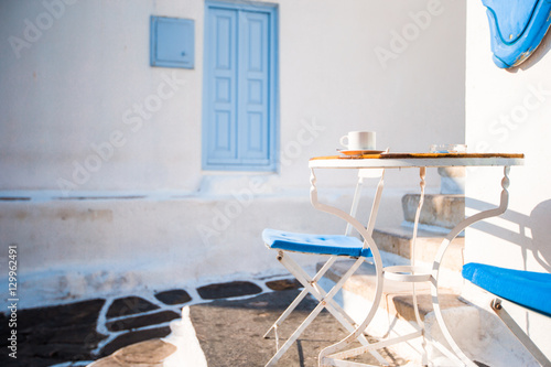 Fototapeta Naklejka Na Ścianę i Meble -  Beautiful cafe on a street of typical greek traditional village on Mykonos Island, Greece. Coffee on table for breakfast
