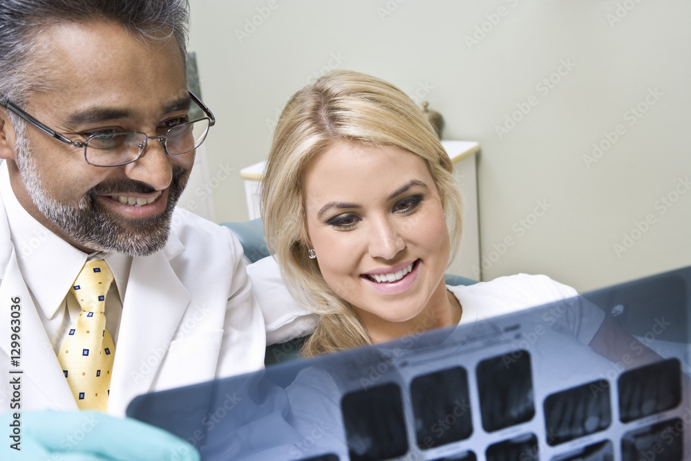 Fototapeta premium Happy dentist with female patient looking at x-ray report at clinic
