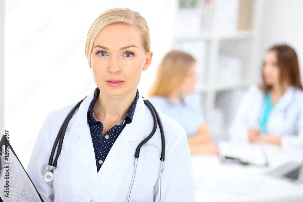 Female doctor smiling on the background with patient and his physician in hospital Female doctor smiling on the background with patient and his physician in hospital