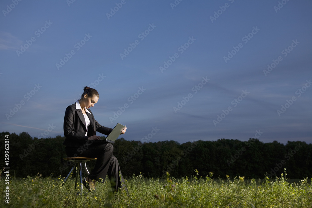 Full length side view of a young businesswoman using laptop in field Full length side view of a young businesswoman using laptop in field