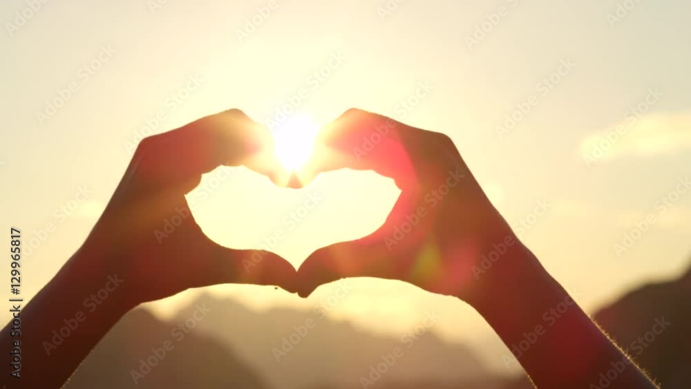 CLOSE UP: Making heart with hands against setting sun and golden evening sky CLOSE UP: Making heart with hands against setting sun and golden evening sky