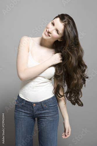 Portrait of a young woman with long brown wavy hair against gray background