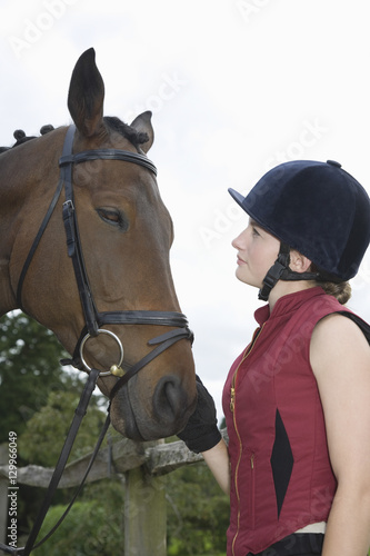 Side view of a young woman in riding hat with a horse outdoors © moodboard