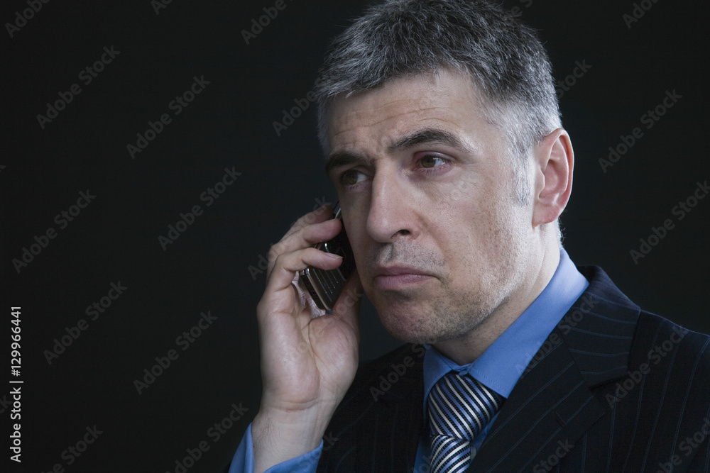Closeup of a serious and worried businessman using cellphone against black background Closeup of a serious and worried businessman using cellphone against black background