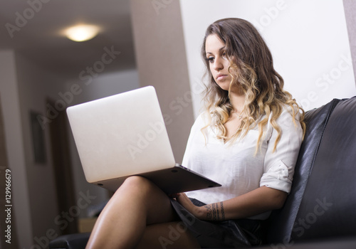 Close-up portrait of beautiful woman using her laptop while sitting on couch and working.