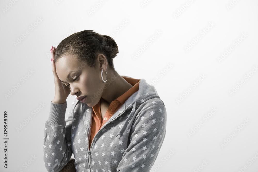 Pensive young woman holding hand on head against gray background Pensive young woman holding hand on head against gray background
